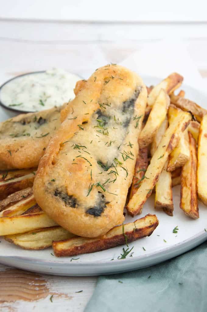 vegan fish made of tofu on a white plate with fries and vegan tartar sauce in the background 