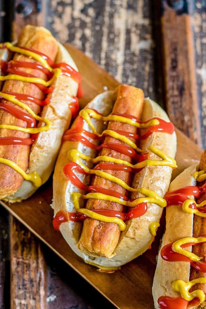 three vegan hot dogs with mustard and ketchup on a wooden board 