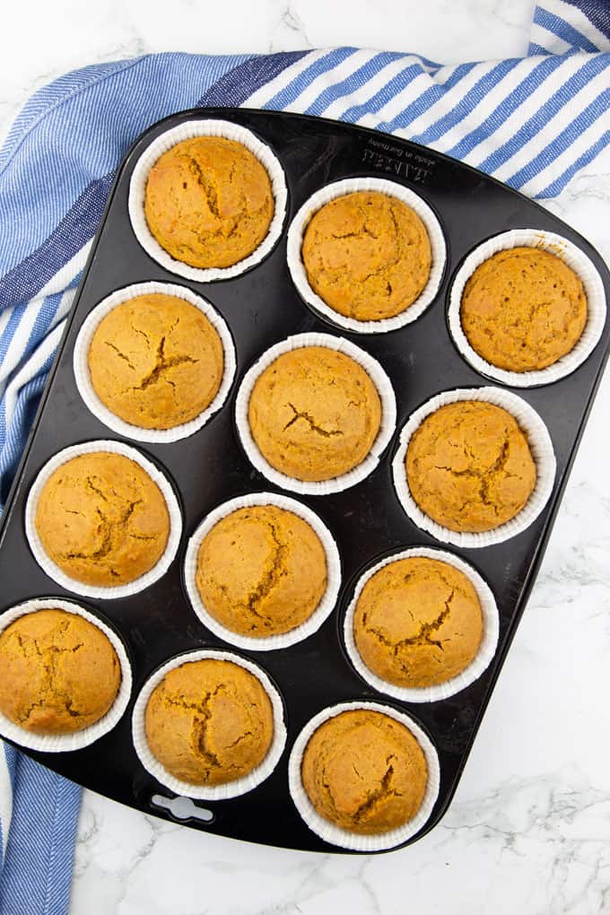 Vegan Pumpkin Muffins in a black muffin pan after baking on a marble countertop 