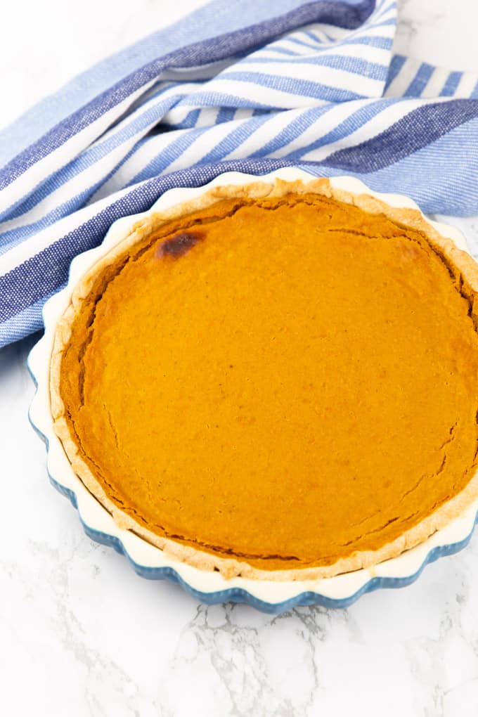 a vegan pumpkin pie in a blue baking form on a marble countertop