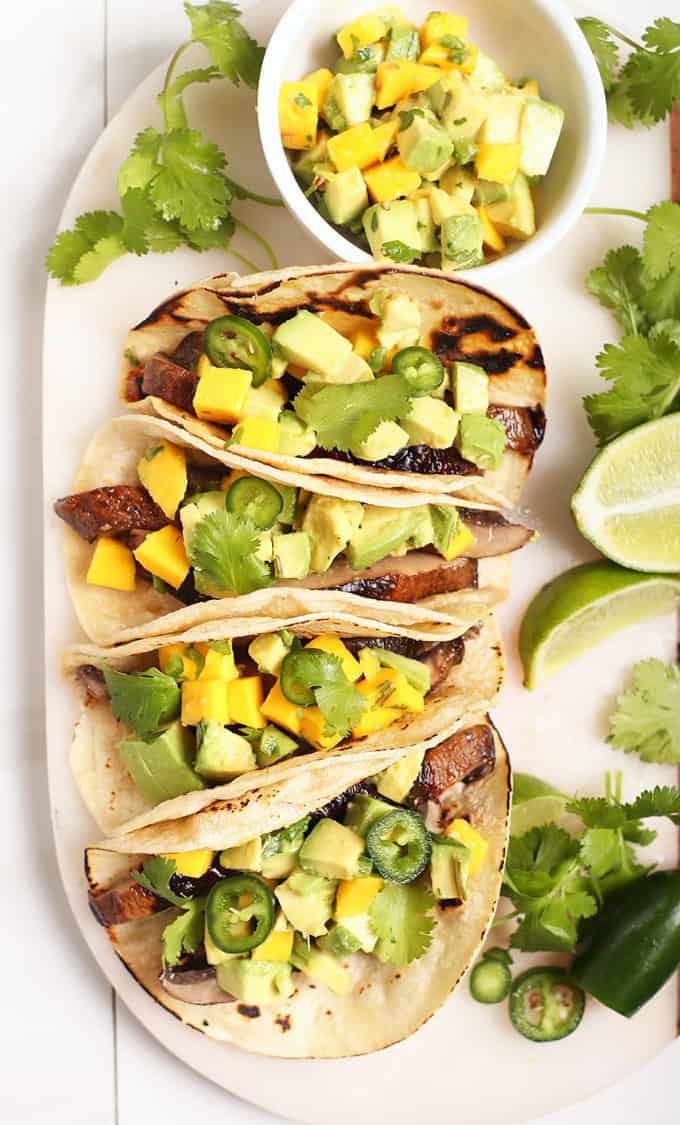 four mushroom tacos with pineapple salsa on a white plate with cilantro and lime halves on the side 