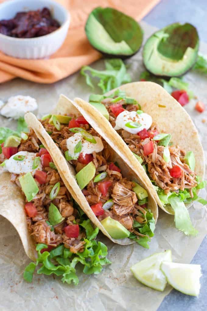 three Jackfruit Tacos on parchment paper with avocado and lime halves on the side 