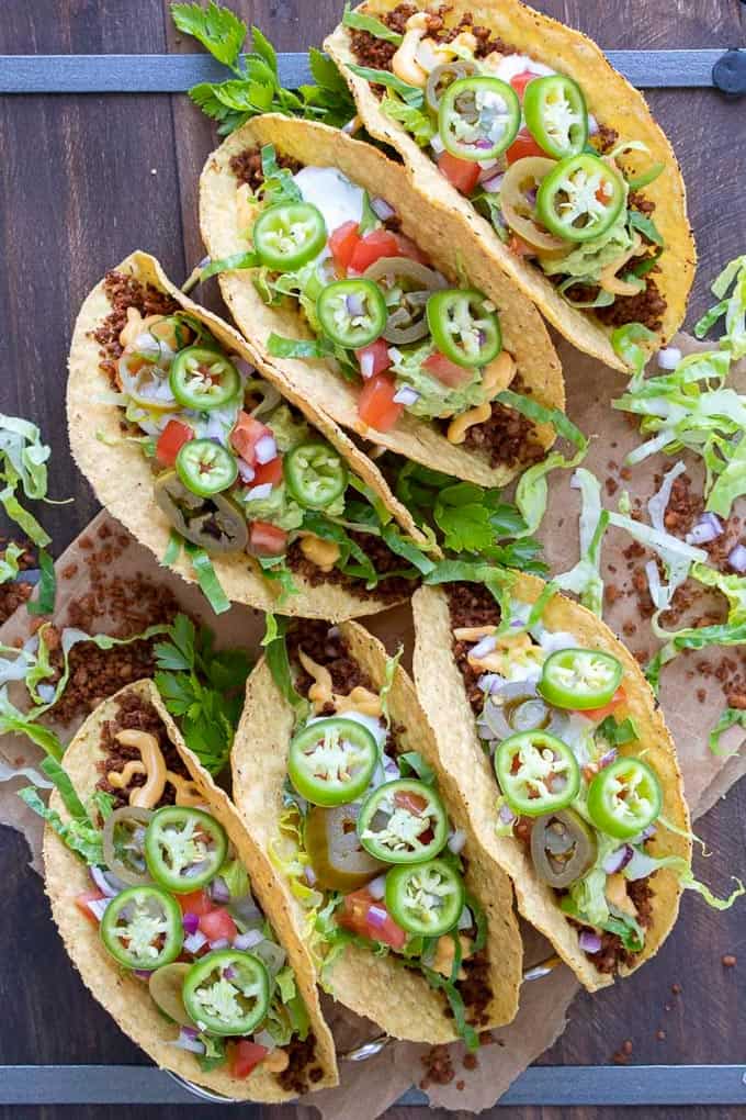 six vegan tacos on a wooden board with jalapeños on top 