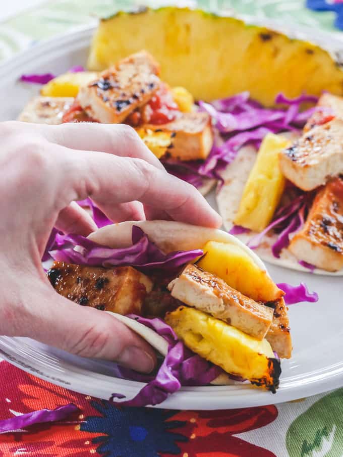 a hand holding Hawaiian Tofu Tacos with Grilled Pineapple on a white plate 