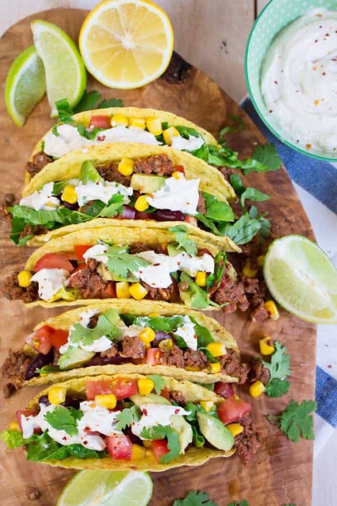 five vegan tacos with lentil walnut meat on a wooden board with lime wedges on the side 