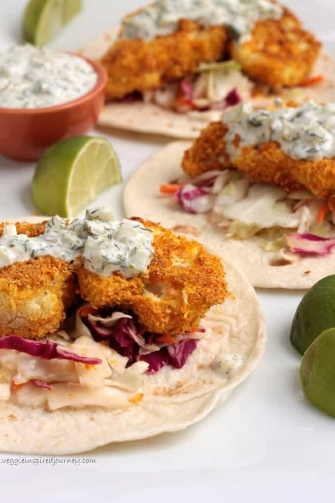 three crispy baked cauliflower tacos on a white countertop with limes on the side 