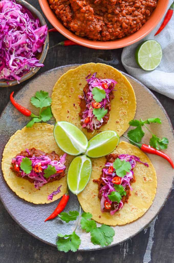 three lentil tacos with lime slaw on a grey plate with fresh cilantro and lime wedges 