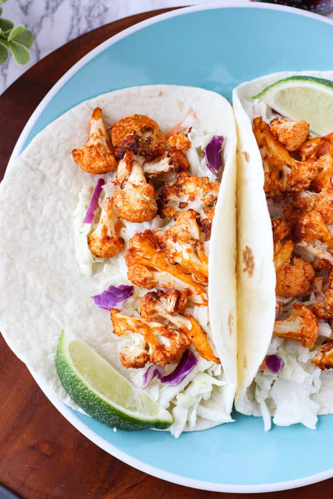 two Vegan Buffalo Cauliflower Tacos with lime wedges on a light blue plate 