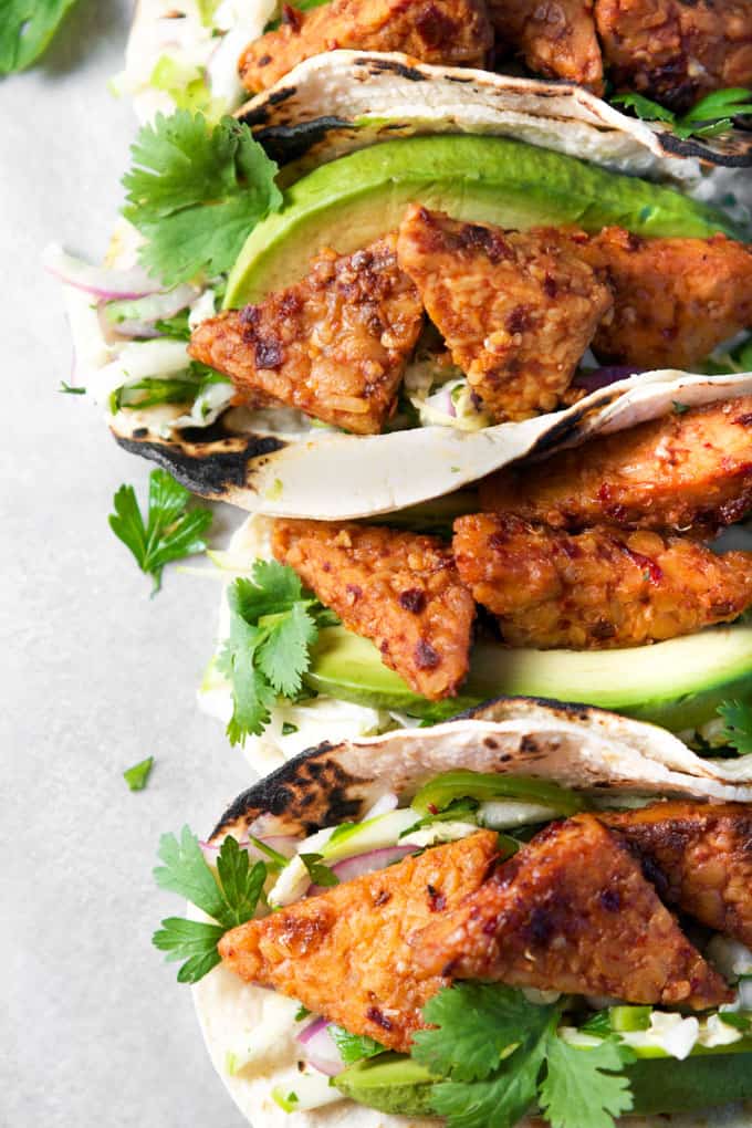 four Spicy Chipotle Tempeh Tacos with Green Apple Slaw on a concrete countertop 