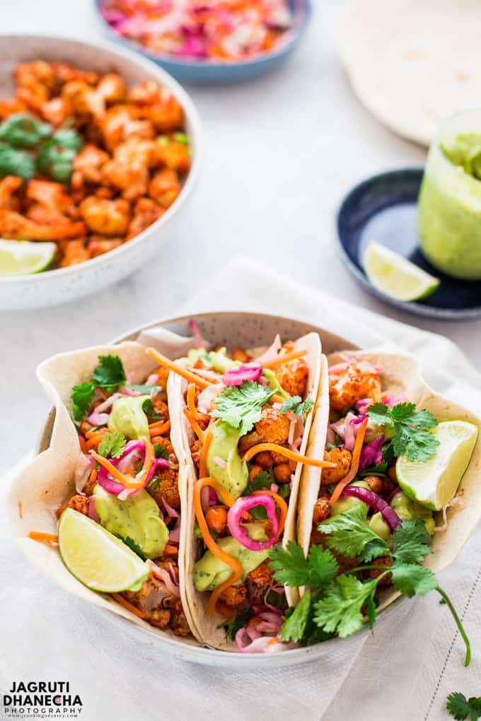 three Tandoori Cauliflower Chickpea Tacos in a white bowl with a bowl of tandoori cauliflower in the background