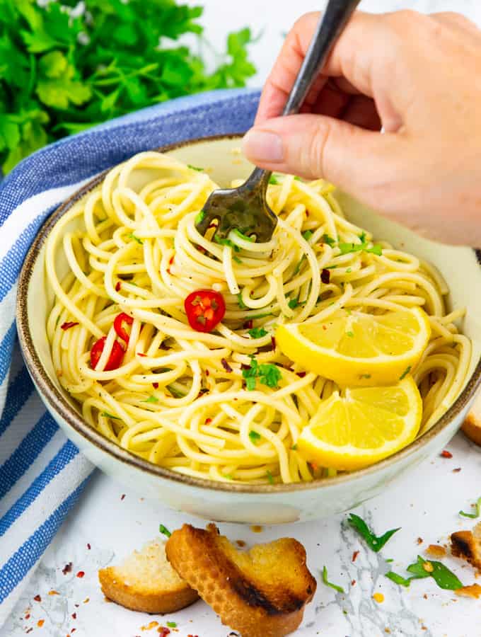 spaghetti aglio e olio in a beige bowl with hand rolling up some of the spaghetti with a fork 