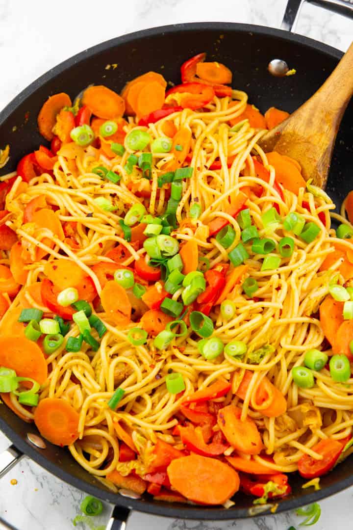 Asian Spaghetti with carrots, red bell pepper, and Chinese cabbage in a black pan with a wooden spoon