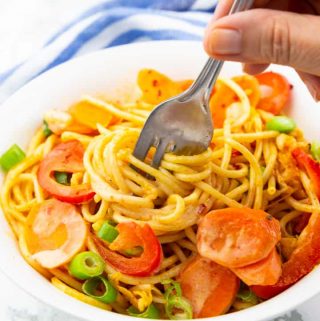 Asian Spaghetti with carrots and red bell pepper in a white plate with a hand rolling up some of the spaghetti with a fork