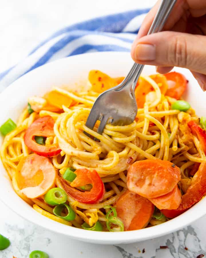 Asian Spaghetti with carrots and red bell pepper in a white plate with a hand rolling up some of the spaghetti with a fork