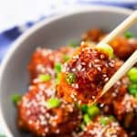 Broccoli Wings in a grey bowl sprinkled with sesame seeds and green onion rings with two chopsticks picking up one of the wings