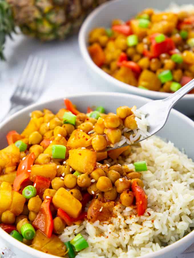 Two Bowls of Sweet and Sour Chickpeas over Rice on a marble countertop with a fork picking up some of the chickpeas 