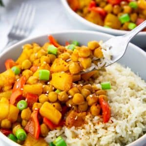 Two Bowls of Sweet and Sour Chickpeas over Rice on a marble countertop with a fork picking up some of the chickpeas