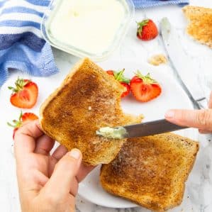 a hand holding toast and spreading vegan butter with strawberries on the side
