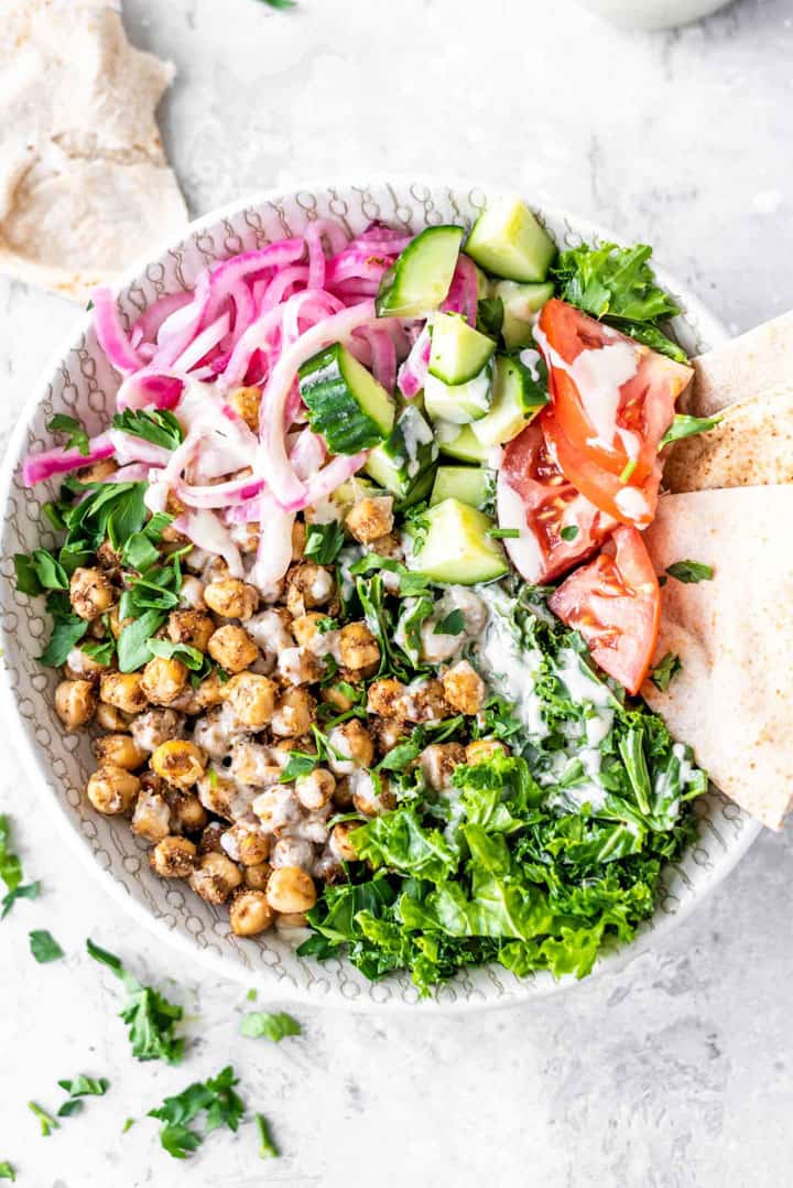 Chickpea Shawarma Salad on a concrete countertop with pita bread and fresh herbs on the side
