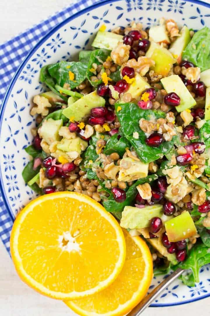 lentil salad with spinach and pomegranate in a white and blue bowl with two orange slices on top