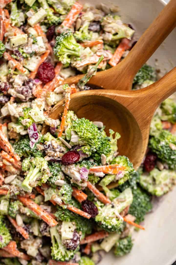 Crunchy Broccoli Salad in a white bowl with two wooden spoons 