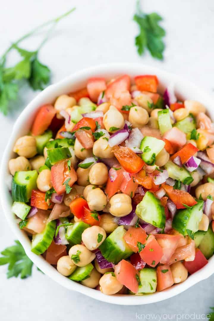 Chickpea Salad with tomatoes and cucumbers in a white bowl on a white countertop with fresh parsley on the side