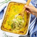 Vegan Scalloped Potatoes in a white baking dish with a hand holding a wooden spoon with scalloped potatoes