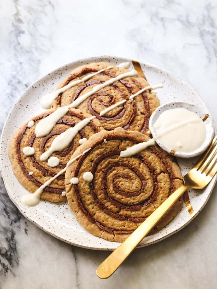 three cinnamon roll pancakes on a white plate with a fork on the side 