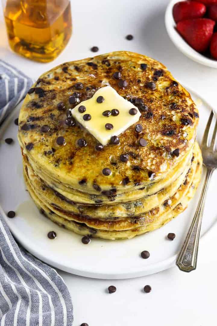 a stack of vegan pancakes with chocolate chips on a white plate with a piece of butter on top and a fork on the side 