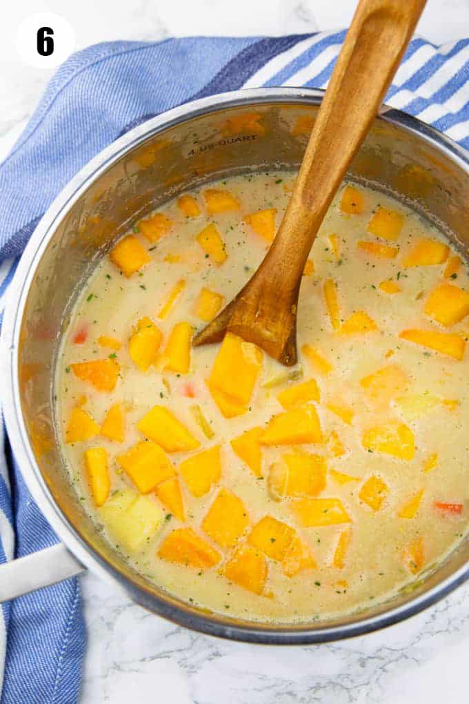 pumpkin soup in a pot with a wooden spoon before blending 