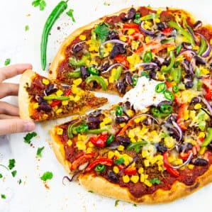 a Mexican pizza on a marble countertop with a hand taking a slice