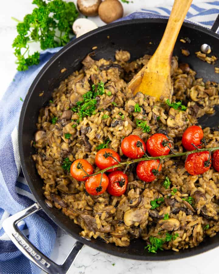 vegan mushroom risotto in a black pan with roasted cherry tomatoes