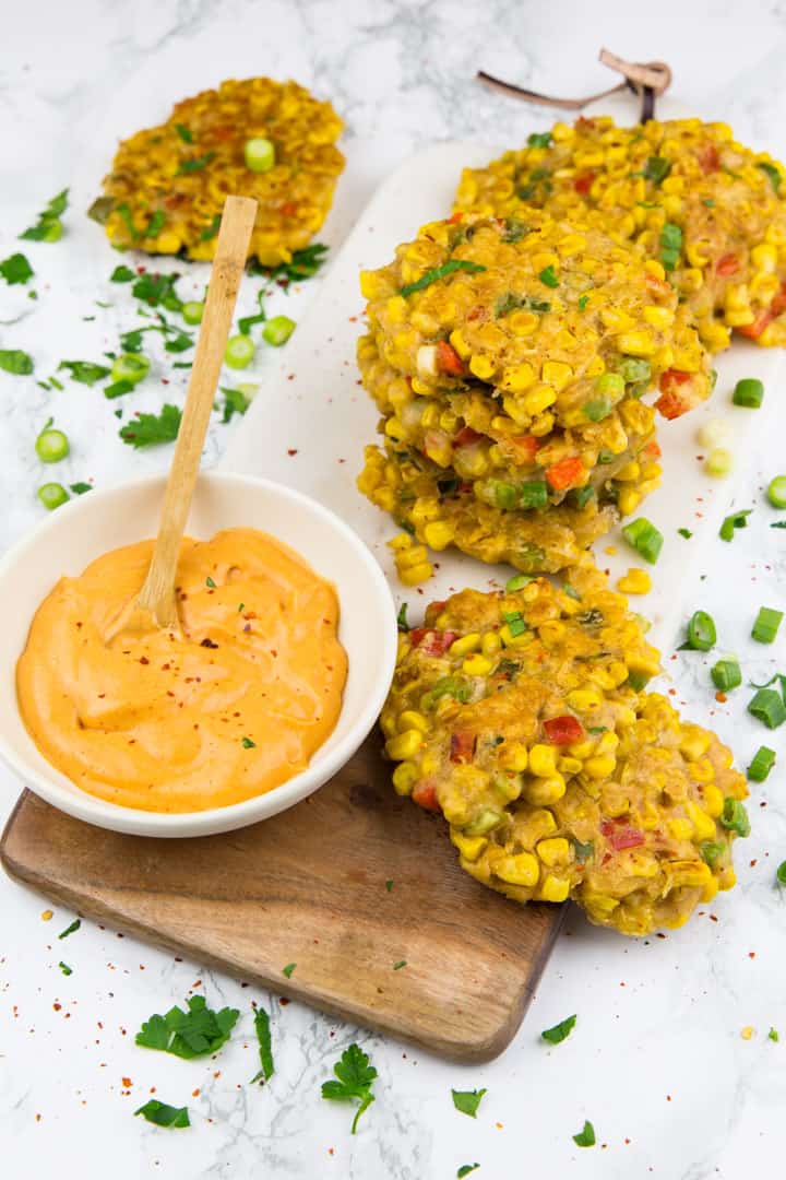 corn fritters on a wooden serving board on a marble countertop with a bowl of paprika mayonnaise on the side