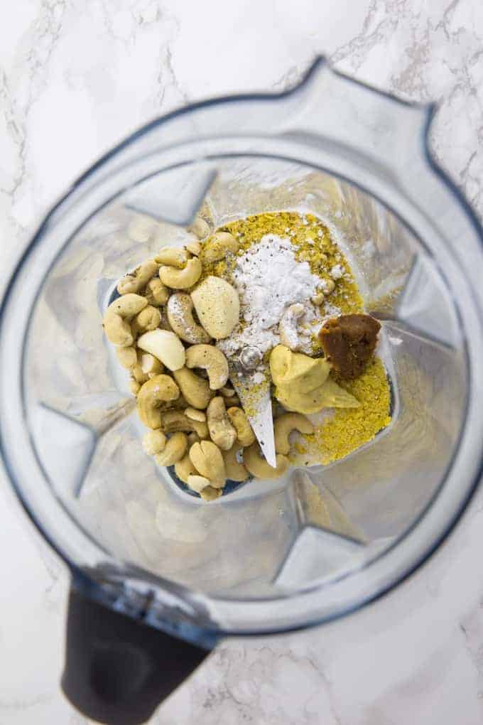 cashews, garlic, nutritional yeast. miso paste, and mustard in a blender on a marble countertop
