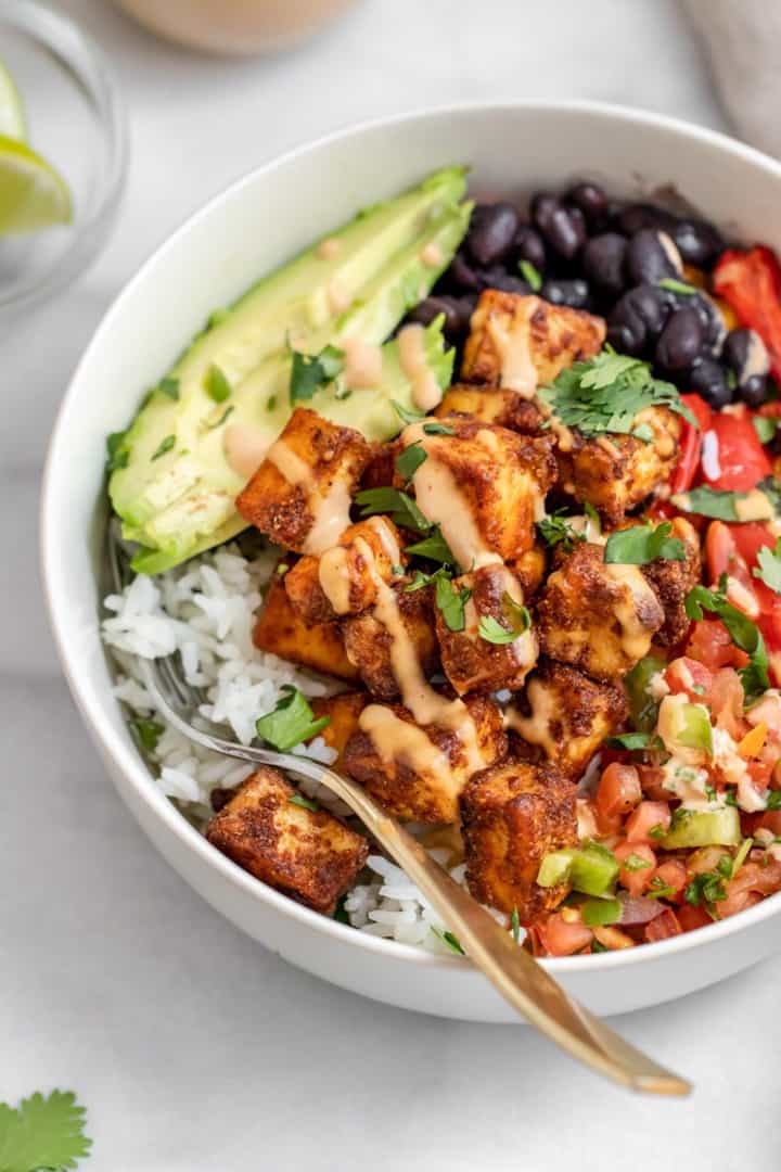 a bowl with rice, tempeh, black beans, and avocado on a white countertop 