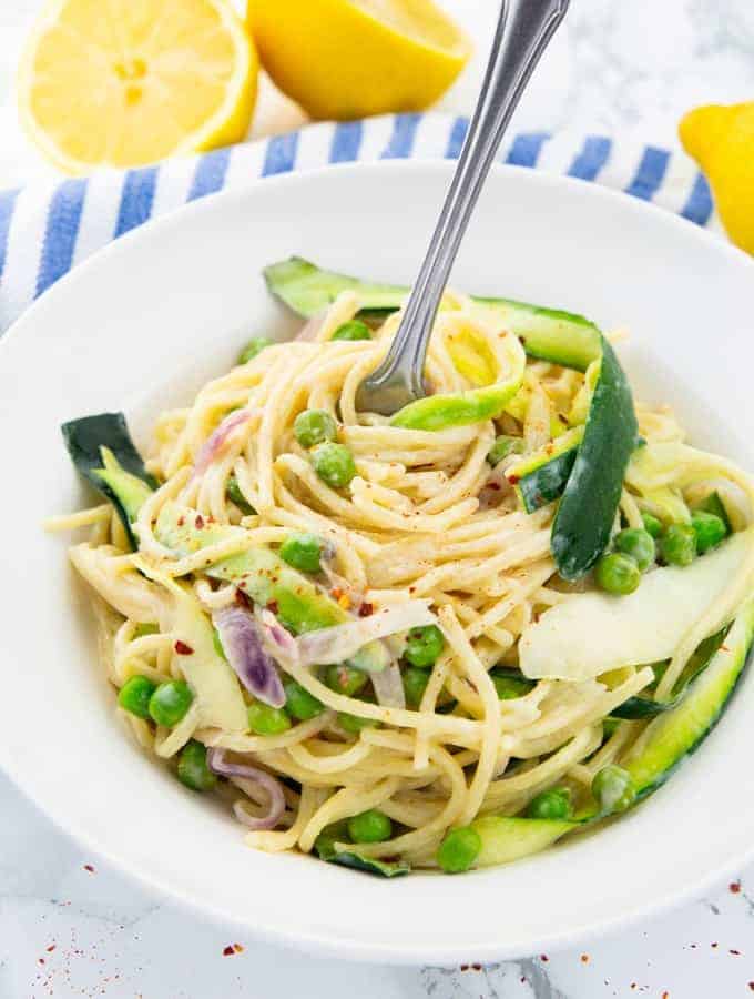 a white plate with lemon zucchini spaghetti on a marble countertop with lemon halves in the background 