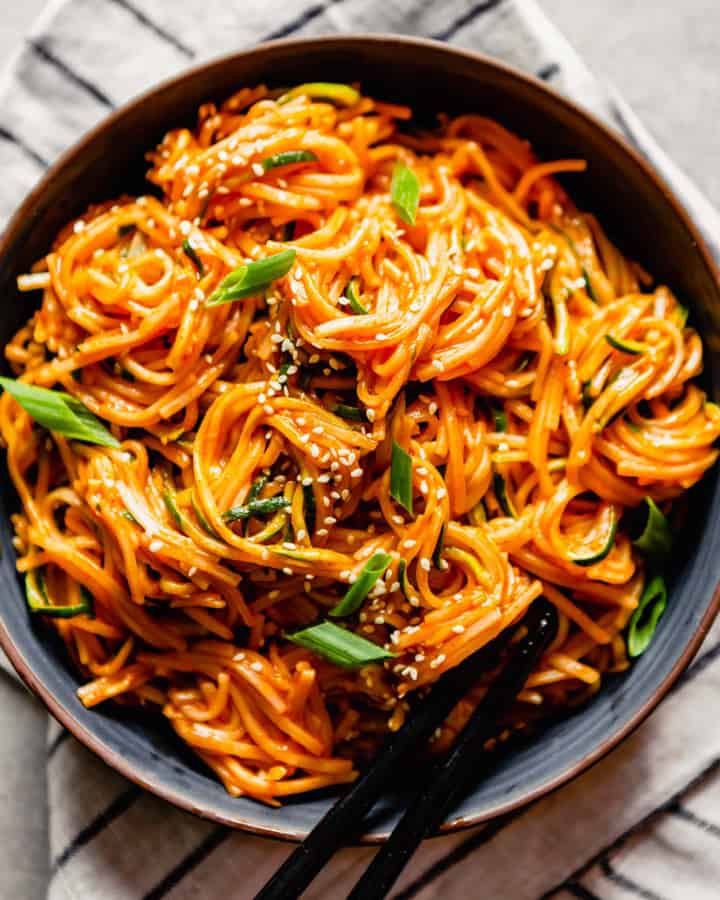 a black plate with Saucy Gochujang Noodles with black chopsticks 