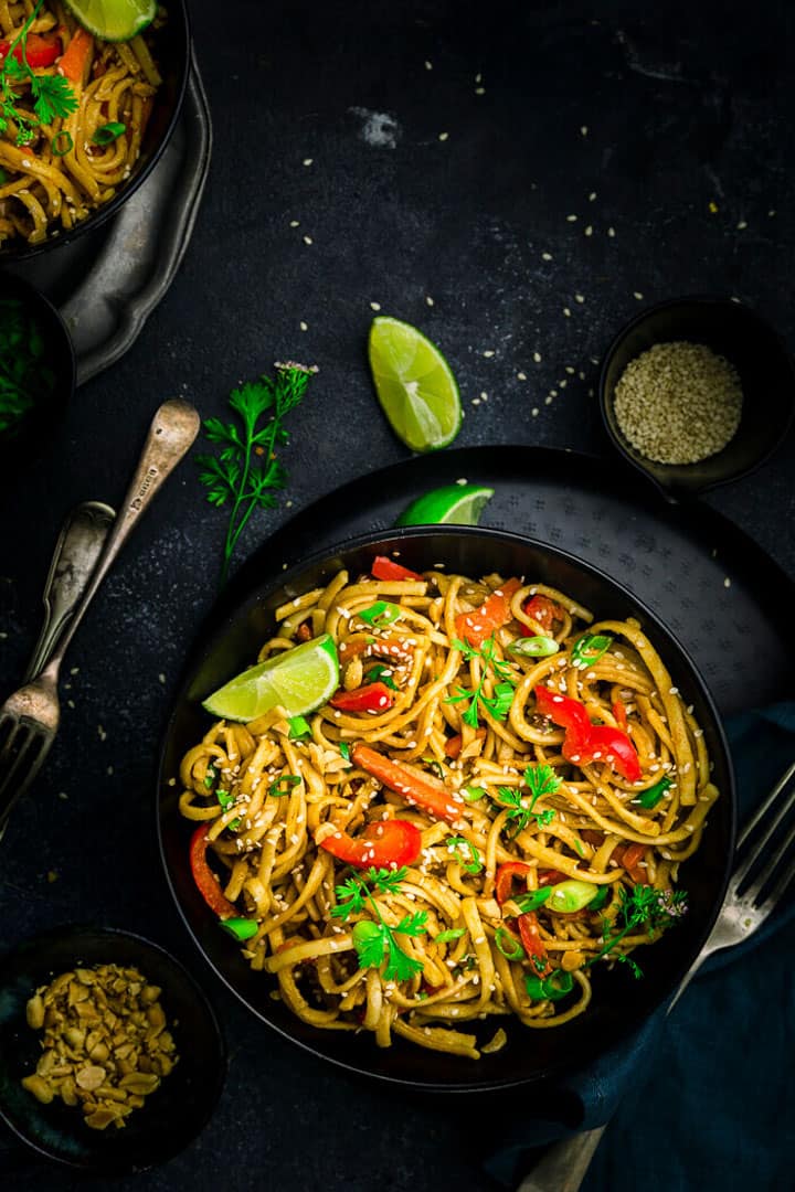 a black bowl with Instant Pot Thai Peanut Noodles on a dark countertop with lime halves in the background