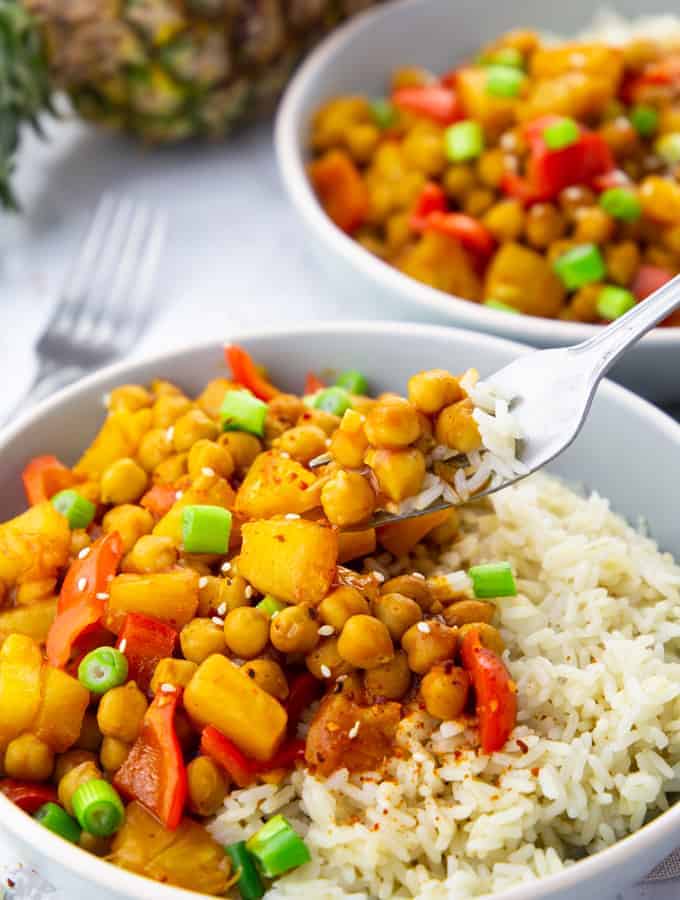 two bowls with rice and sweet and sour chickpeas with a pineapple in the background