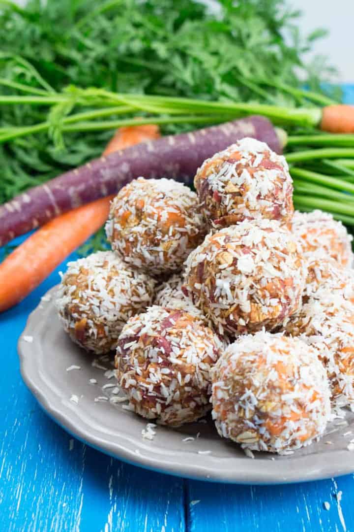 a plate with a stack of carrot cake energy balls with on a blue wooden board with carrots in the background