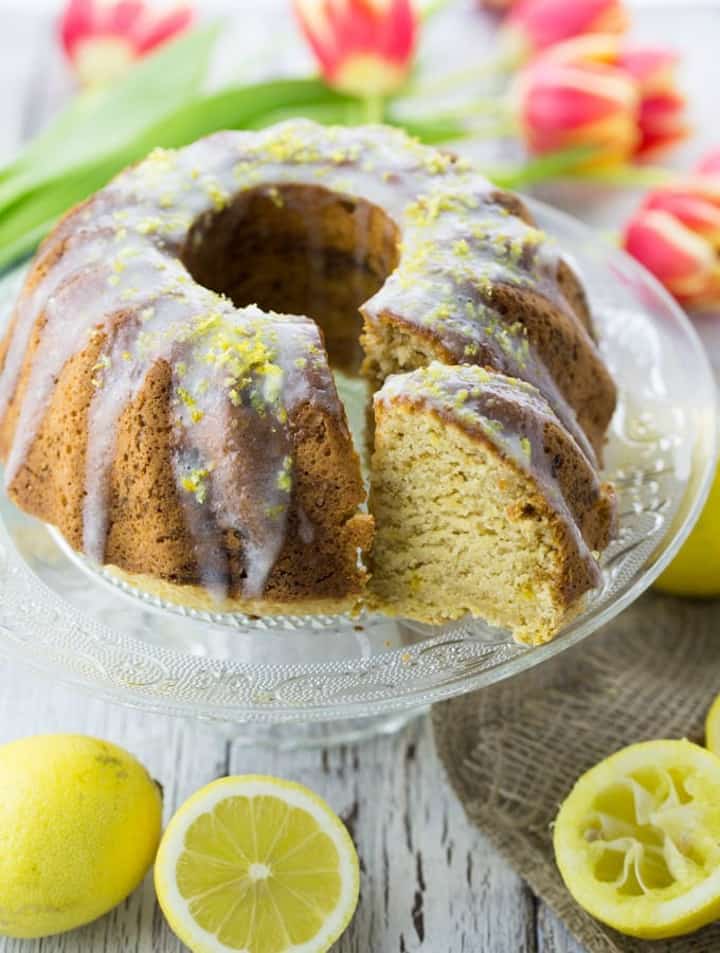 a vegan lemon cake on a cake platter with tulips in the background 