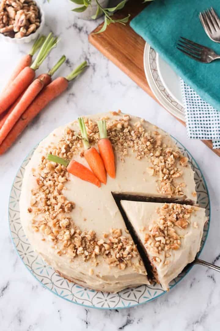 a vegan carrot cake on a marble countertop with carrots on the side 