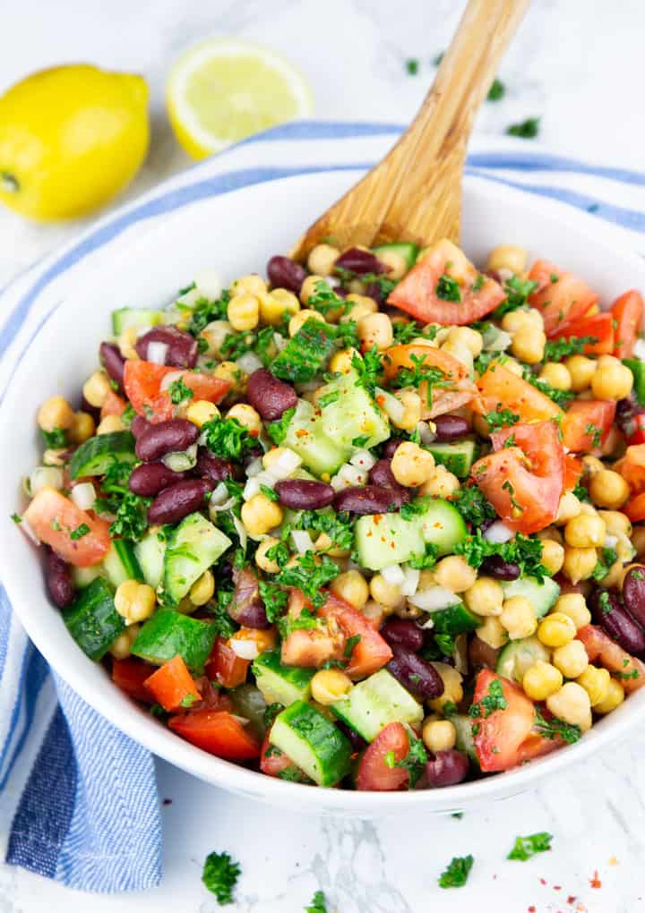 Chickpea Salad in a white bowl with a wooden spoon and two lemons in the background