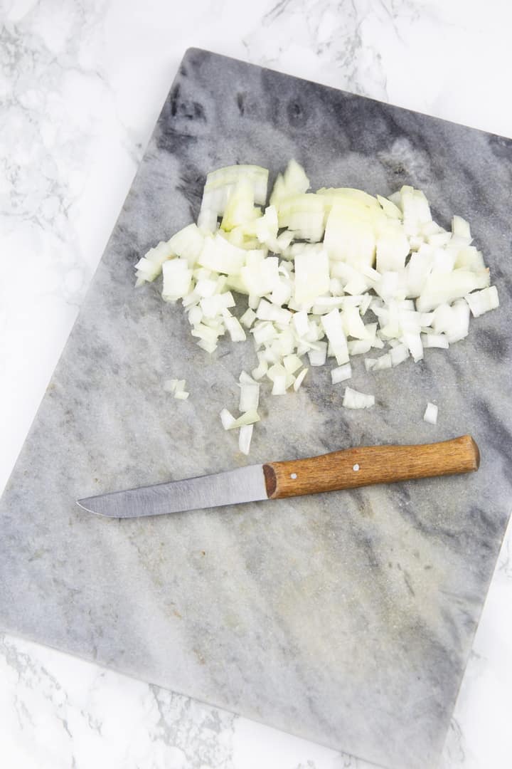 diced Spanish onion on a chopping board with a knife on the side 