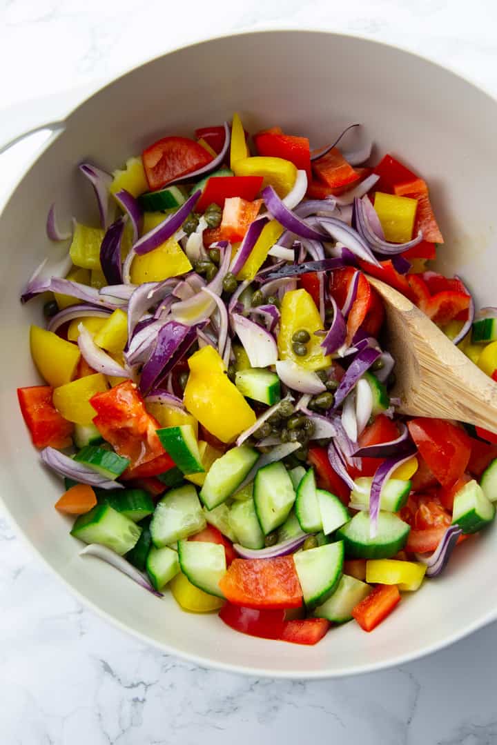 roughly chopped tomatoes, cucumber, bell pepper, and a red onion in a large grey bowl on a marble countertop 