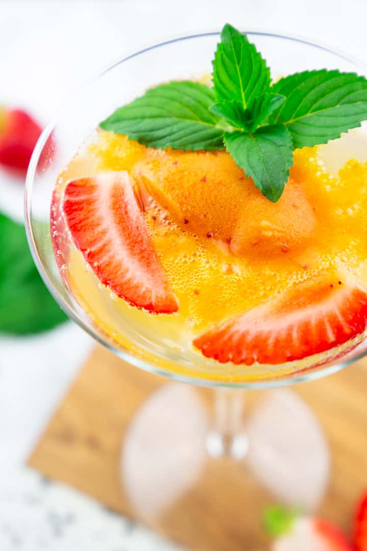 a close-up photo of a glass of champagne with sorbet, two strawberry halves, and mint 