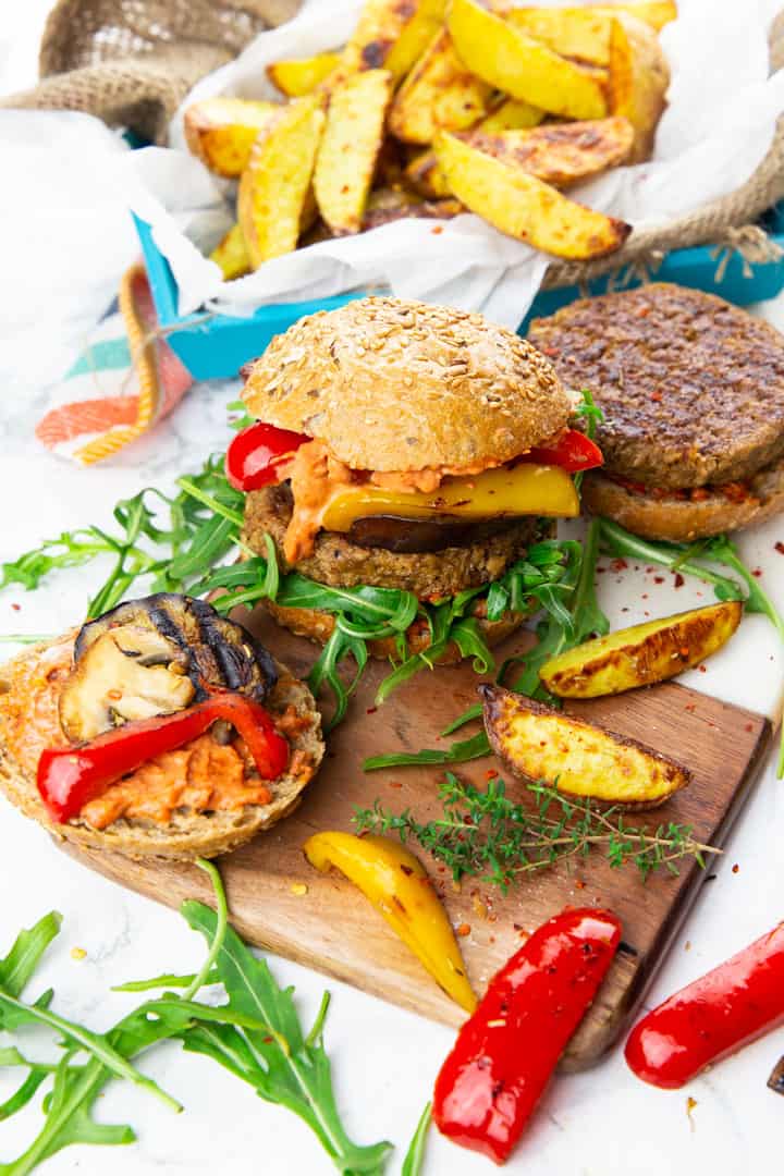 a burger with a seitan patty, grilled vegetables, and arugula on a wooden board 