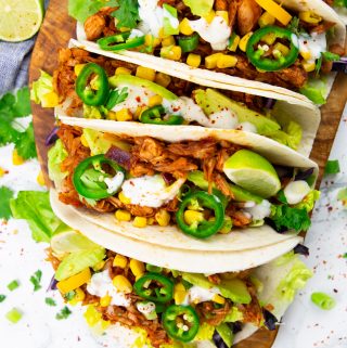 tacos filled with pulled jackfruit, lettuce, and corn on a wooden board
