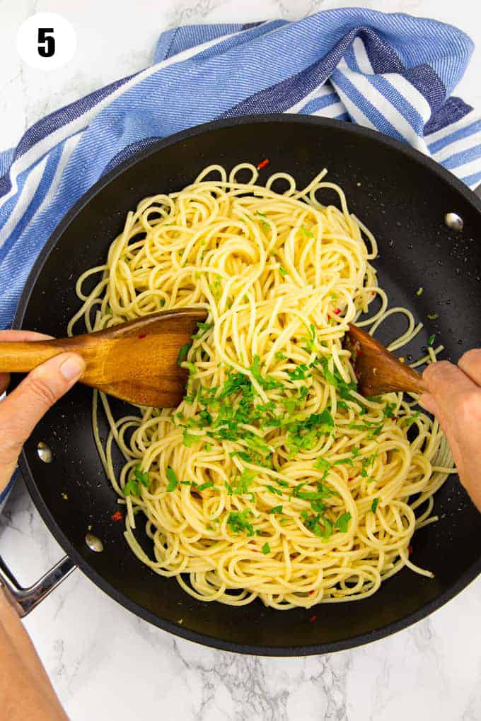 spaghetti in a black pan with two hands tossing them 