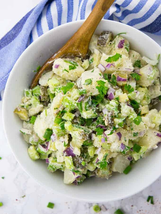 a white bowl with potato salad and a wooden spoon on a marble countertop with a blue dishcloth in the background 